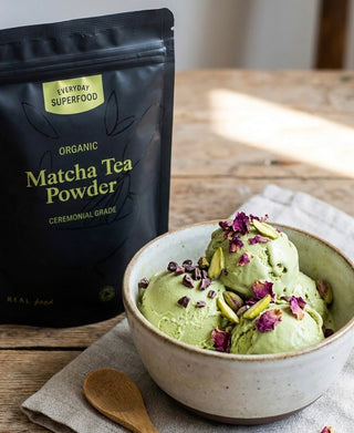 Creamy matcha ice cream topped with pistachios, rose petals, and cacao nibs beside Everyday Superfood Organic Matcha Tea Powder.